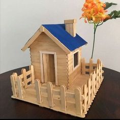 a small wooden house sitting on top of a table next to a vase with an orange flower