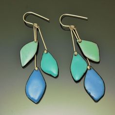 two pairs of blue and green earrings on a gray surface with gold earwires