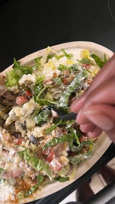 a person cutting into a salad on top of a white plate with black tongs