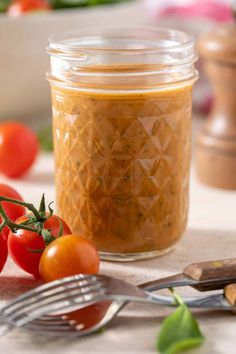 a glass jar filled with tomato sauce next to a fork and some tomatoes on the table