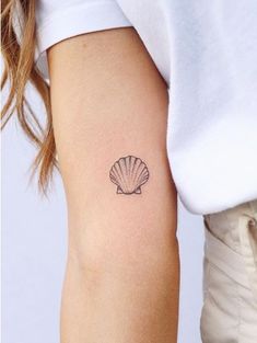 a woman's arm with a small shell tattoo on the left side of her right arm