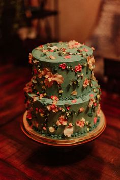 a three tiered green cake with flowers on the top is sitting on a wooden table