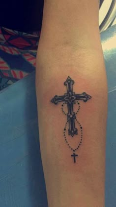 a cross tattoo on the arm with a bead around it and an arrow in the middle