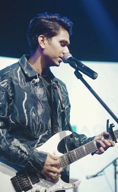 a young man holding a guitar and singing into a microphone