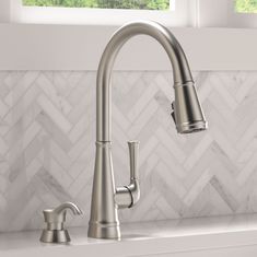 a kitchen faucet with two handles on the sink and marble backsplash