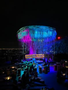 people are sitting at tables in front of an illuminated structure