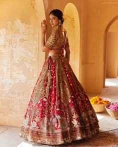 a woman in a red and gold bridal gown standing next to a wall with flowers