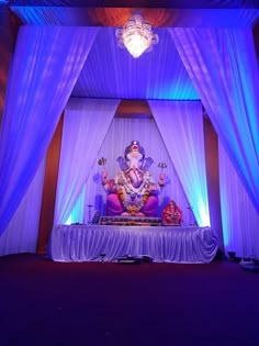 an idol sitting on top of a table under a purple lit stage with white drapes