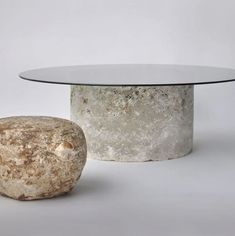 a round glass table sitting next to a rock on top of a white floor covered in dirt