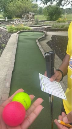 two people holding tennis balls and a pen in their hands on a miniature golf course