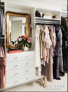 an organized closet with clothes and shoes on the shelves, mirror above it and vase full of flowers