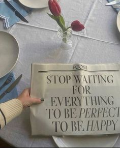 a person is holding up a newspaper on a table with plates and silverware in front of them