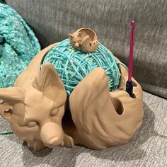 a ceramic figurine sitting on top of a couch next to a ball of yarn