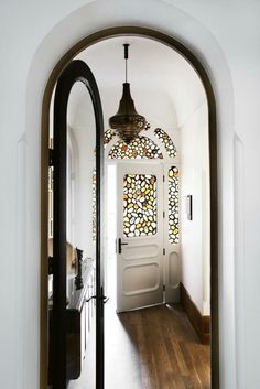 an arched doorway leading to a hallway with stained glass panels on the wall and wooden floors