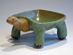 a ceramic turtle shaped bowl with one foot in the shape of a turtle sitting on it's side