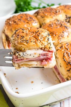 ham and cheese sliders in a white baking dish with a fork sticking up from the side