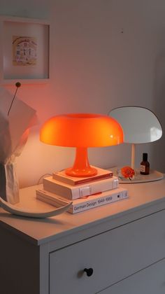 an orange lamp sitting on top of a white dresser next to a stack of books