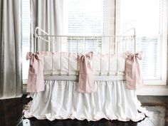 a crib with pink and white ruffled bedding in front of a window