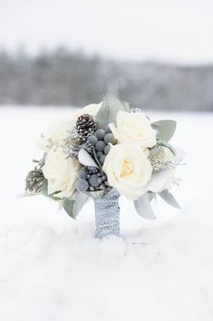 a bridal bouquet in the snow with pine cones and berries on it's side