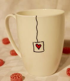 a white coffee cup with a heart drawn on the side and some raspberries scattered around it