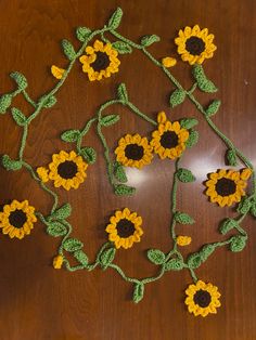 crocheted sunflowers are arranged on a wooden surface with green stems and leaves