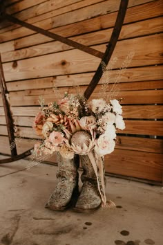 a cowboy boot with flowers in it is sitting on the ground next to a wooden wall