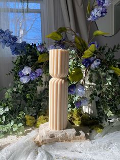 a tall vase sitting on top of a table next to blue flowers and greenery