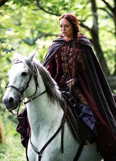 a woman dressed in medieval garb riding a white horse