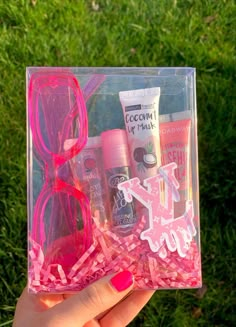 a person holding up a clear box with pink items in it and some grass behind them