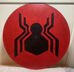 a red disk with black spider - man on it sitting on a white surface next to a wall