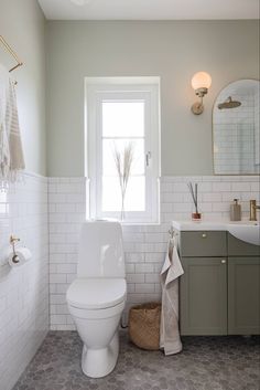 a white toilet sitting in a bathroom next to a sink under a window with towels hanging on it