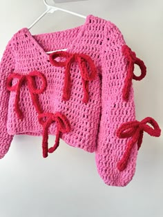 a crocheted sweater hanging on a clothesline with red yarn and bows attached to it