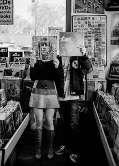 black and white photograph of two people standing in front of a store holding up cds