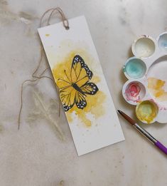 a card with a yellow butterfly on it next to some paint and watercolors