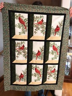 a person holding up a quilt with red birds on it