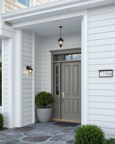 the front door of a white house with two potted plants on each side and an address sign above it