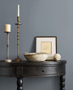 a table with two candles, a bowl and pictures on the wall next to it