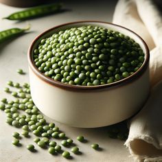 green peas in a bowl on a table next to pea pods and a cloth napkin