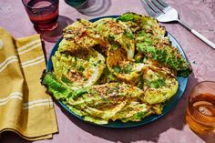 a blue plate topped with lettuce covered in seasoning next to glasses and utensils