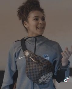 a woman is smiling and holding her purse in one hand while wearing a nike hoodie