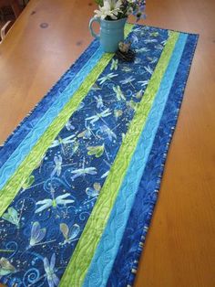 the table runner has flowers in a vase on it and is next to a blue mug