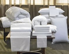 white linens and pillows are stacked on a coffee table