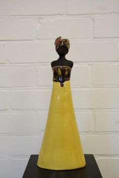 a yellow vase sitting on top of a black table next to a white brick wall