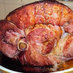 a large ham sitting on top of a wooden table next to a pan filled with meat