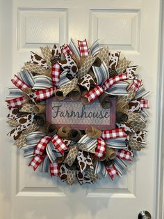 a wreath that says farmhouse on it with red, white and blue ribbons hanging from the front door