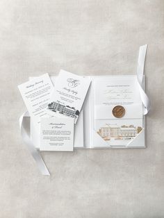 an open pocketfold wedding card with a gold coin on top and white ribbon around it