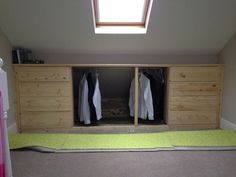 an attic bedroom with clothes hanging on the closet doors and carpeted flooring in front of it