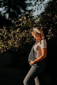 a pregnant woman standing in front of a tree