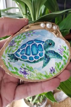 a hand holding a small shell with a sea turtle painted on it's side