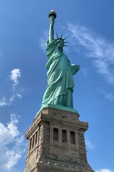 the statue of liberty is shown against a blue sky with wispy white clouds